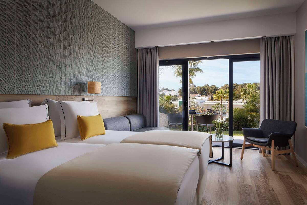 Een hotelkamer met twee bedden, een bureau, een stoel en een balkon met uitzicht.
