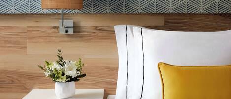 Une chambre à coucher bien rangée, avec une tête de lit en bois, une table de chevet avec une lampe, une commode blanche et un coussin jaune.