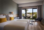A hotel room with two beds, a sofa, a chair, and a balcony with a view of the city.