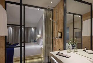 A modern hotel room with a large bed, a bathroom with a shower, and a vanity with toiletries.