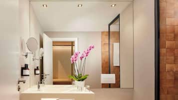 Un baño moderno con un espejo grande, dos lavamanos, una orquídea en maceta y luces empotradas en el techo.