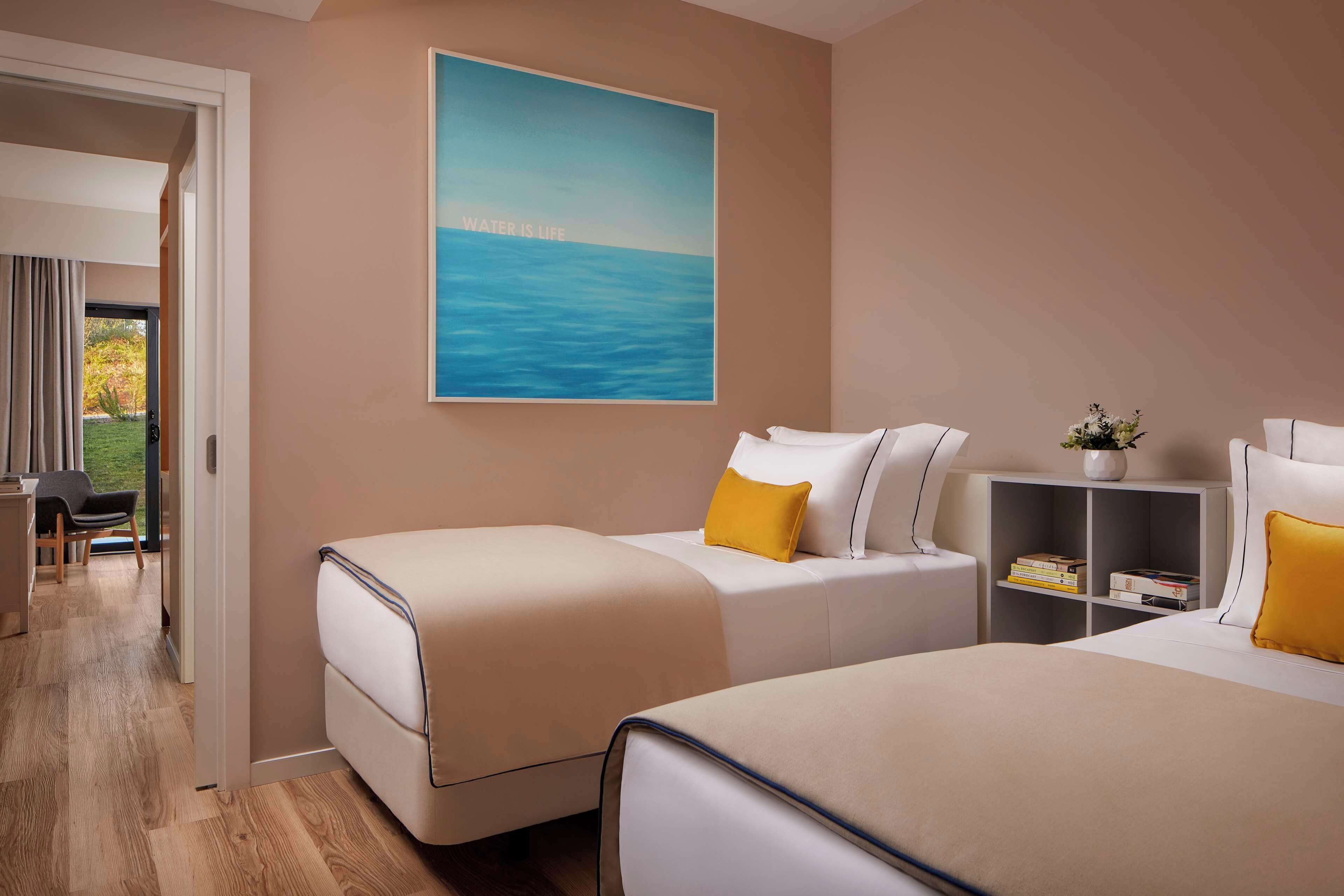 A hotel room with two beds, a bookshelf, a desk, and a large window.