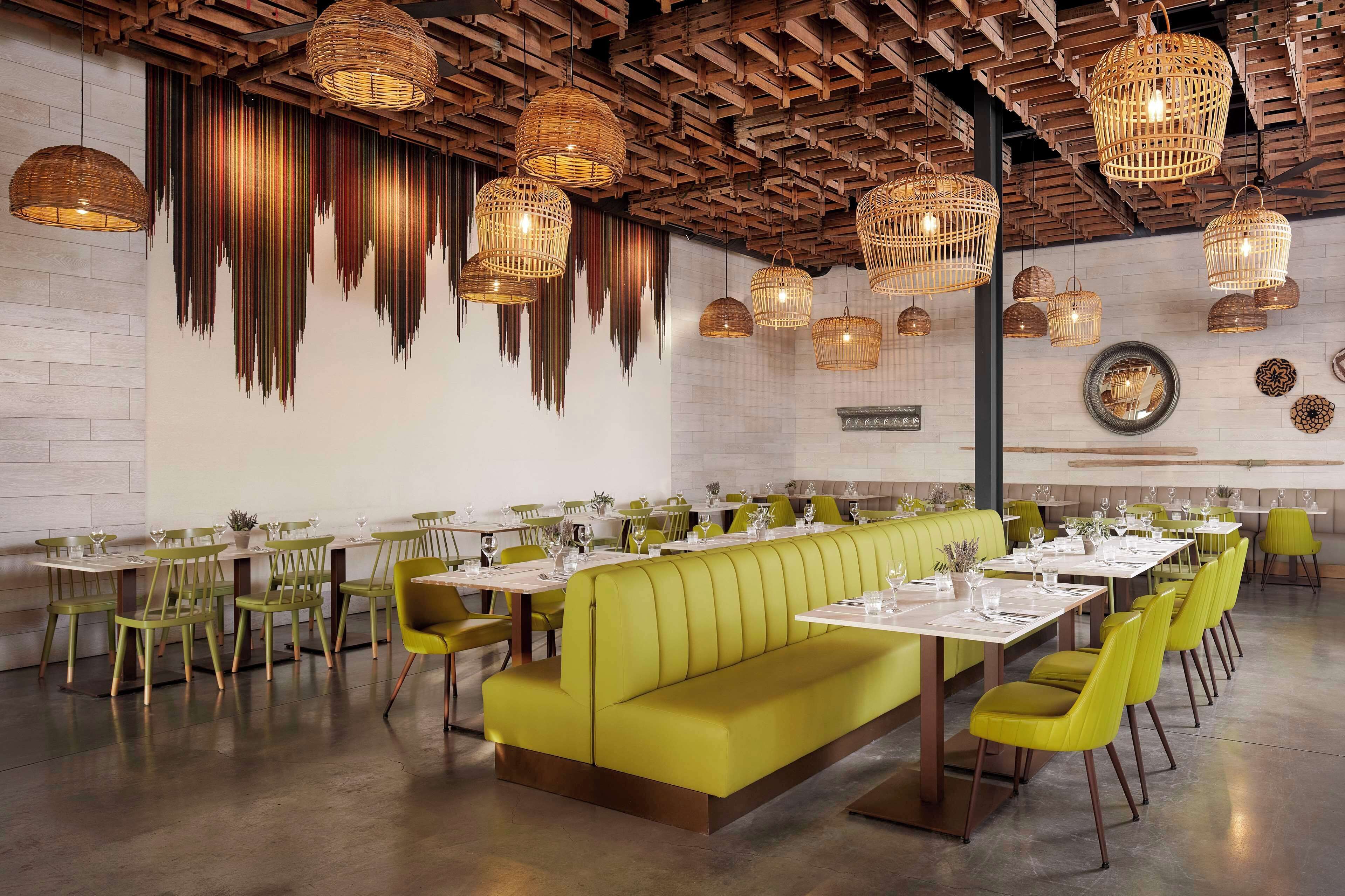 A restaurant with a long green booth, multiple tables, and hanging wicker chandeliers.