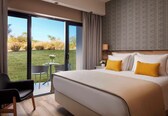 A hotel room with a large bed, a small table, a chair, and a view of the outdoors.