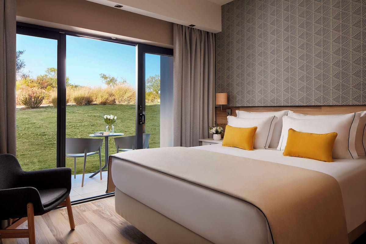 Een hotelkamer met een groot bed, een tafeltje, een stoel en uitzicht op de omgeving.