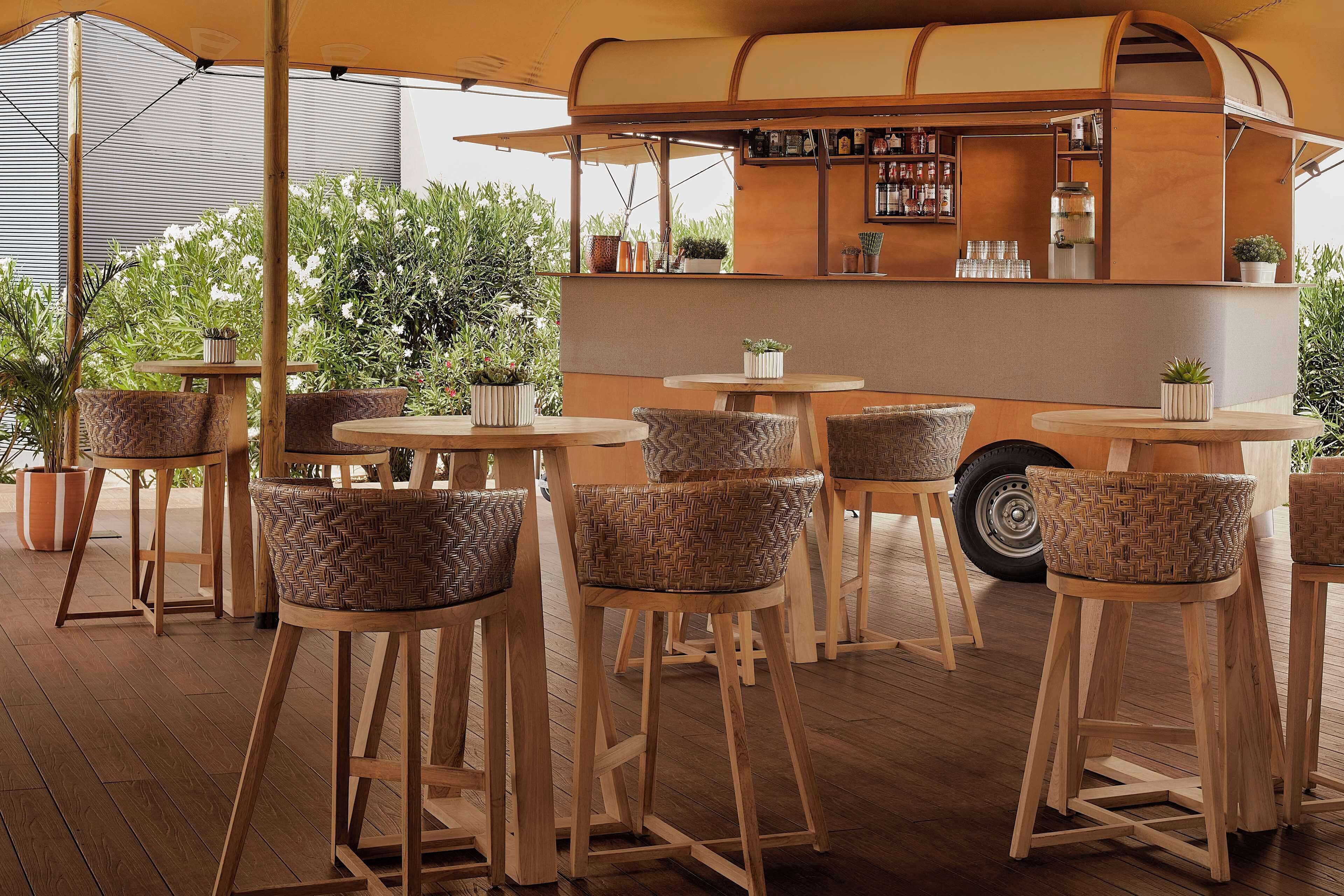 A bar area with wooden stools, a counter with a drink menu, and potted plants.