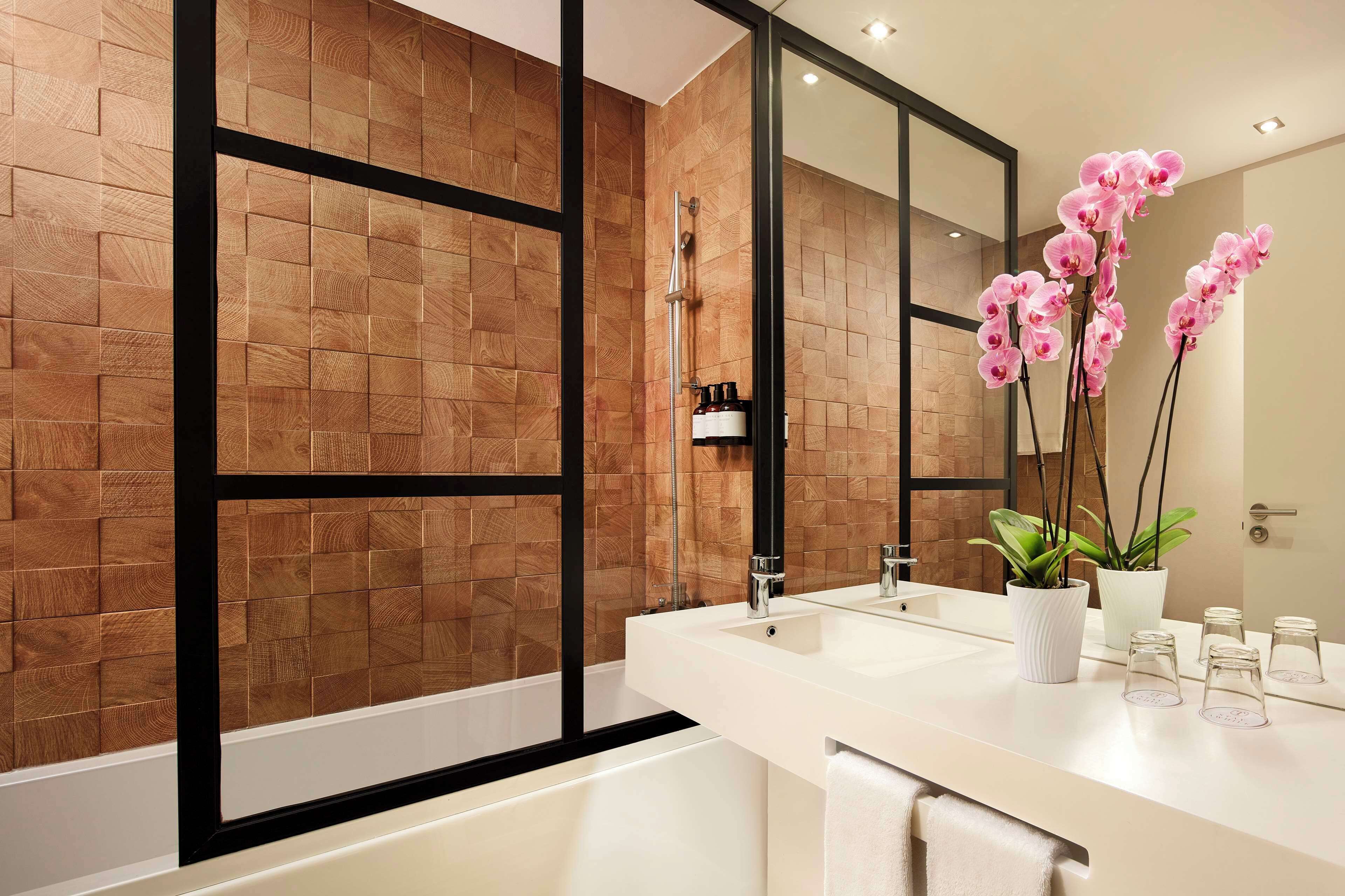 Ein modernes Badezimmer mit Holzwand, großem Spiegel, Badewanne und Waschbecken mit weißer Ablagefläche.