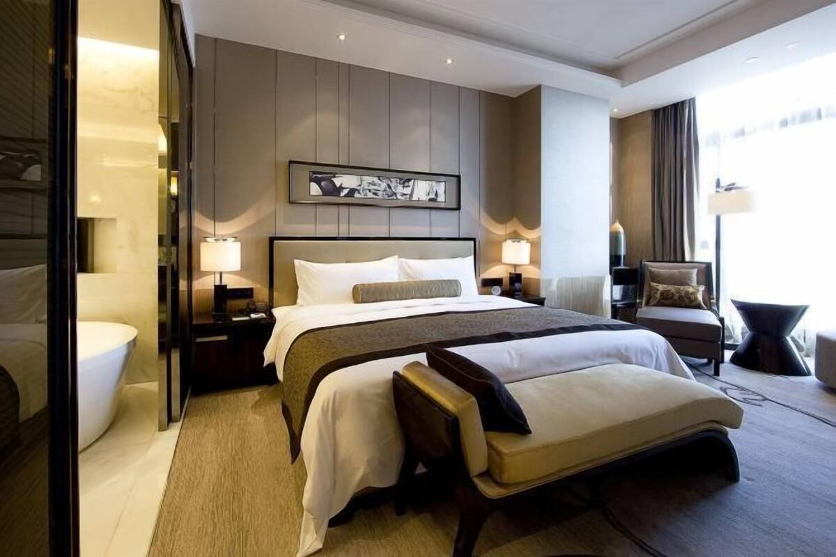 Una habitación de hotel moderna con una cama grande, mesitas de noche, un banco y vistas de la ciudad.