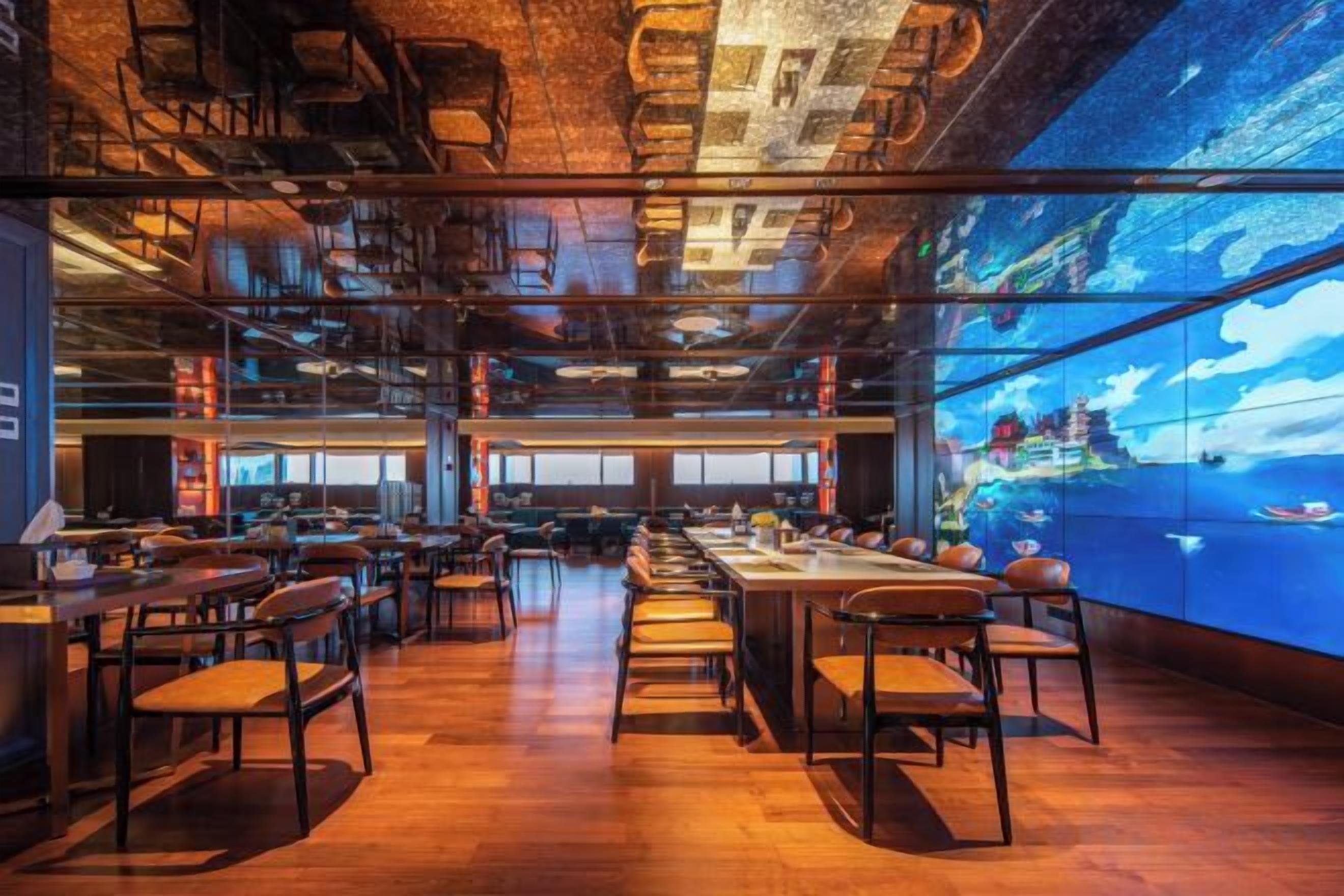 Un restaurante espacioso con techos altos y conductos expuestos, que presenta una gran pantalla digital mostrando una vista panorámica.