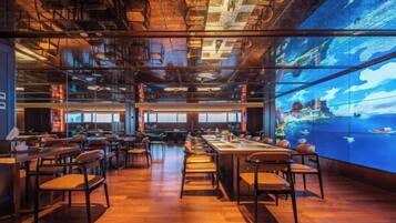 Un restaurante espacioso con techos altos y conductos expuestos, que presenta una gran pantalla digital mostrando una vista panorámica.