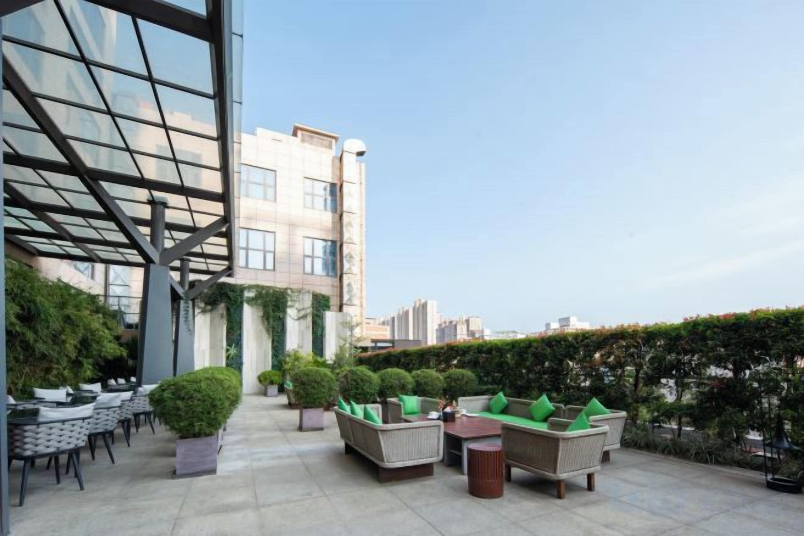 Un área de estar al aire libre con varias mesas y sillas, rodeada de follaje y un edificio con ventanas grandes.