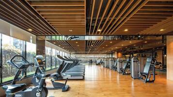 Un gimnasio con equipamiento de ejercicio, suelo de madera y ventanas amplias.