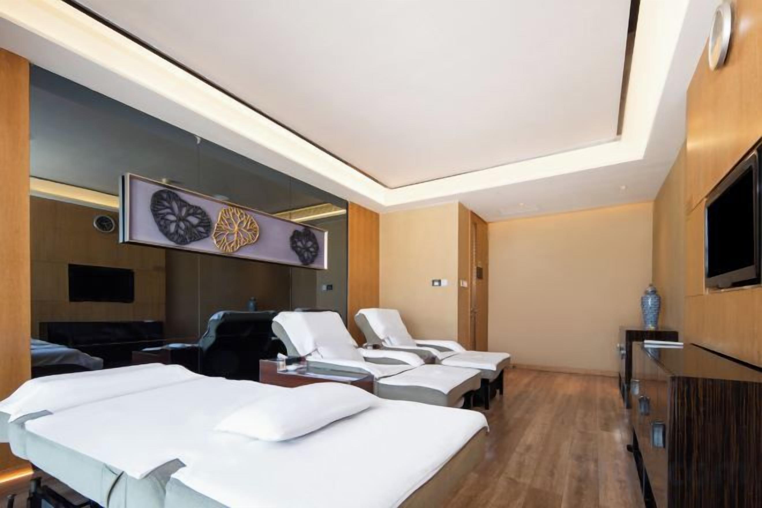 A hotel room with a bed, a TV, a mirror, and a massage chair.