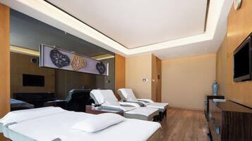 A hotel room with a bed, a TV, a mirror, and a massage chair.