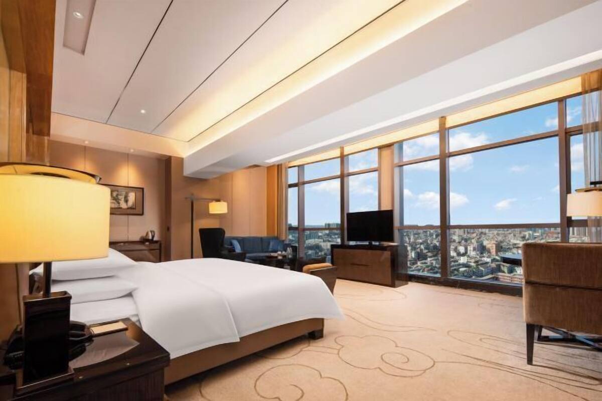 Habitación de hotel con una cama grande, televisión, escritorio y vistas amplias de la ciudad.