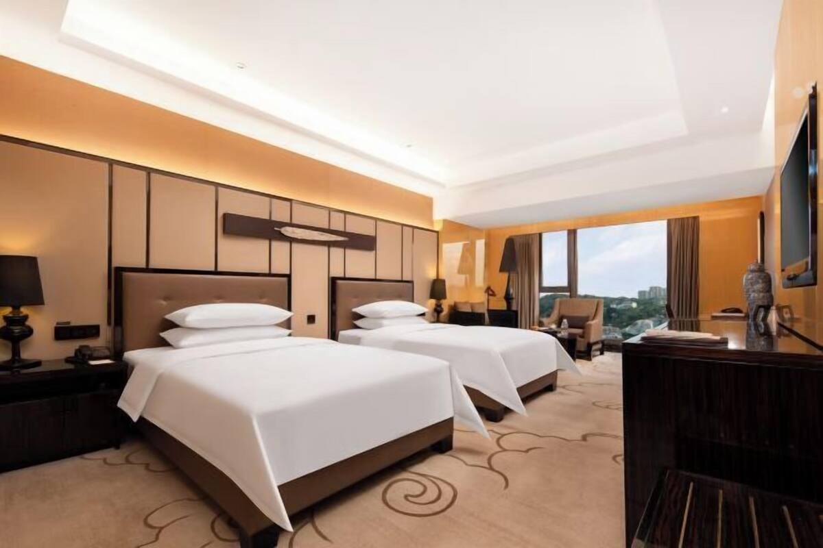 Habitación de hotel con dos camas, un escritorio, una silla y un ventanal con vistas a la ciudad.