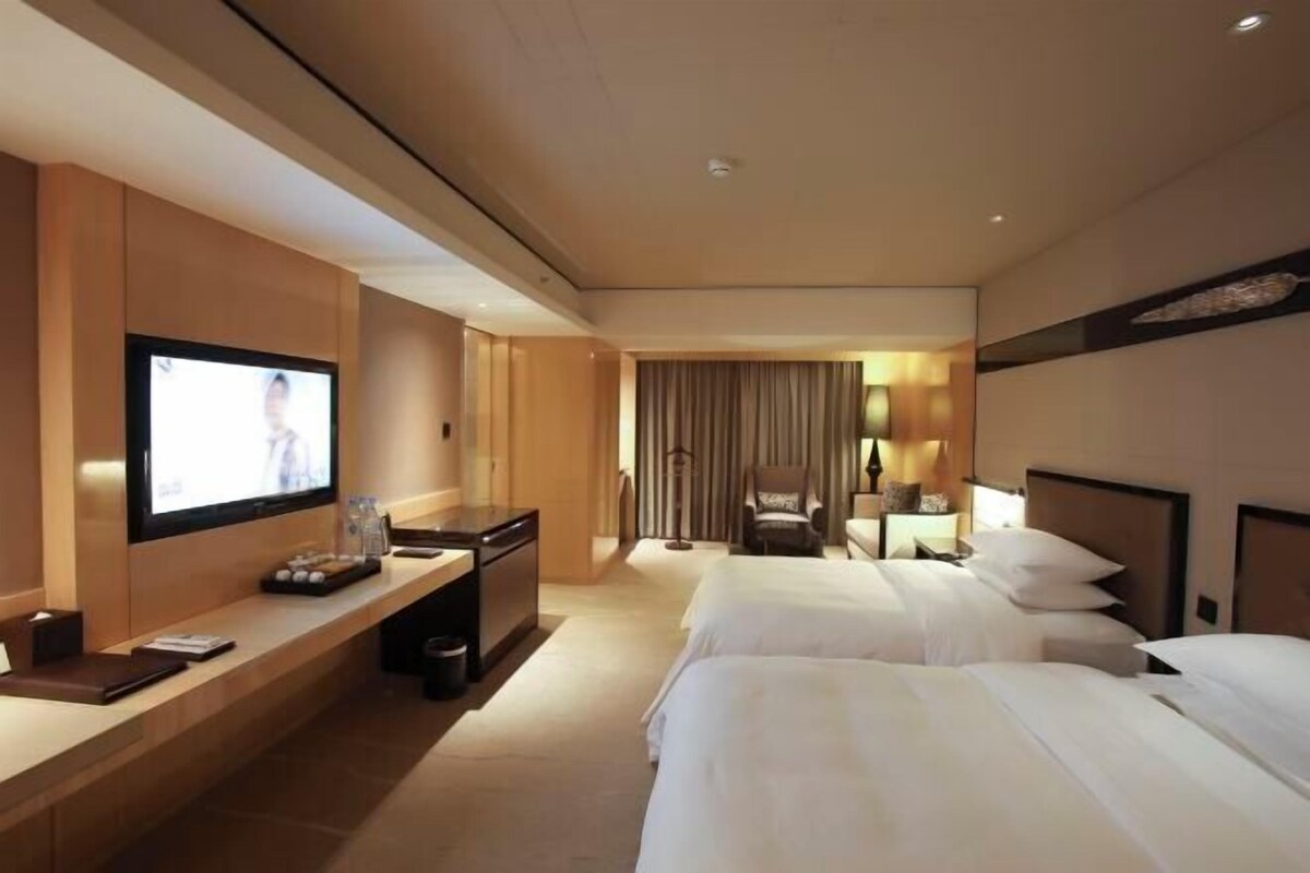 Une chambre d’hôtel équipée d’une télévision, d’un bureau, d’une chaise, de deux lits et d’un rideau.