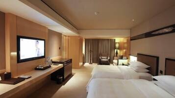 A hotel room with a TV, a desk, a chair, two beds, and a curtain.