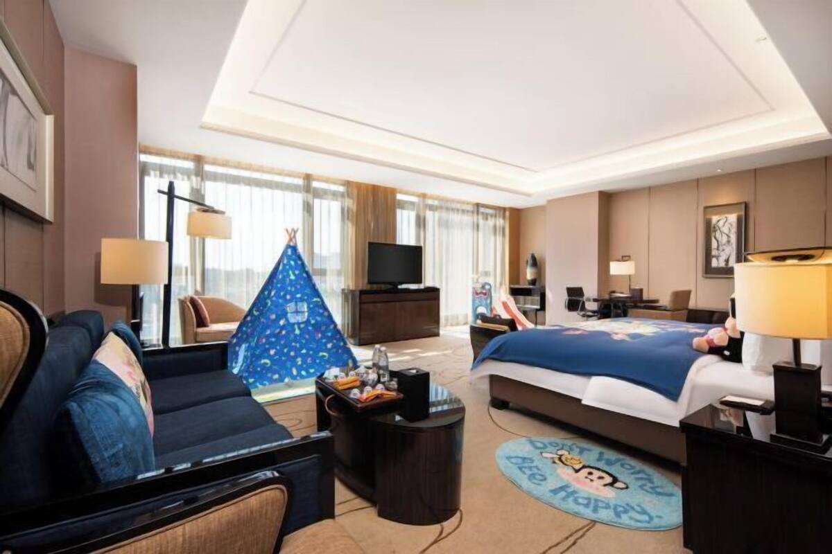 Una habitación de hotel con cama, sofá, televisión, escritorio y lámpara.