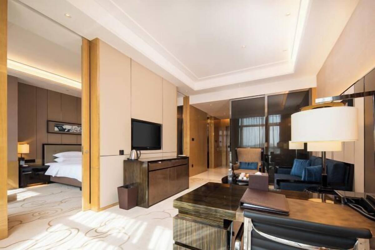 Una habitación de hotel moderna con una cama, un escritorio, un televisor y una zona de estar con sofá y sillones.