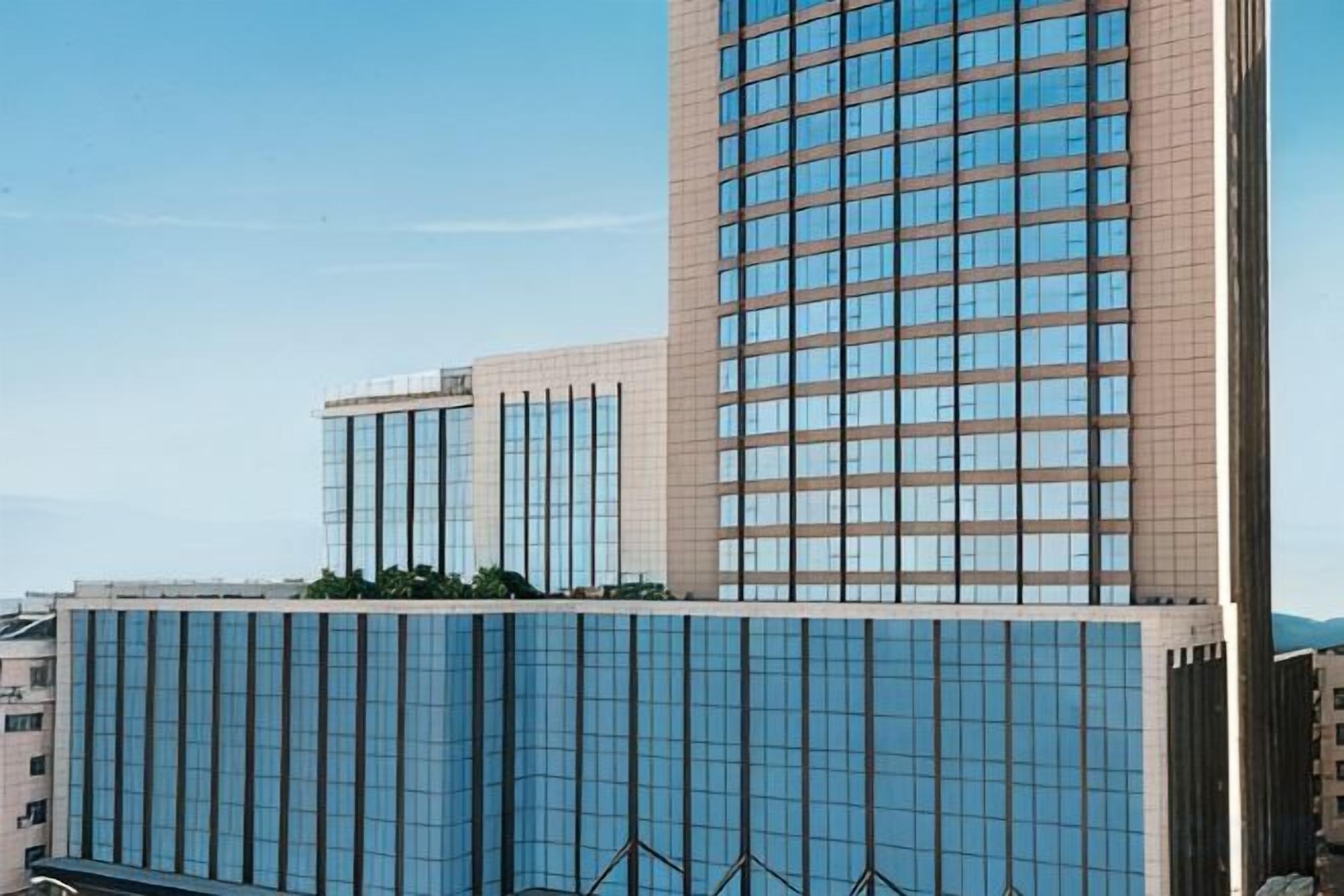 A modern high-rise building with a reflective glass facade, multiple floors, and a clear sky in the background.