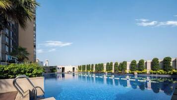 A swimming pool with a clear blue sky, surrounded by greenery and a modern building.