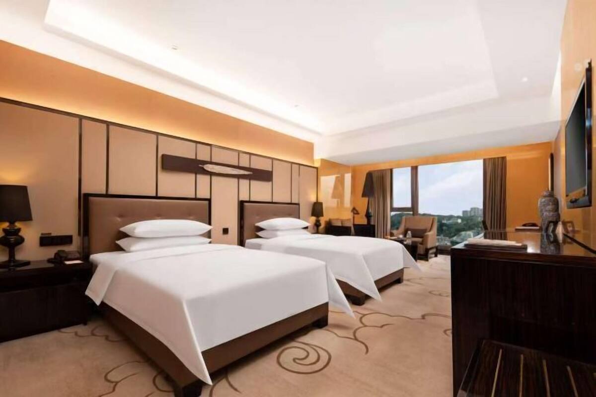 Habitación de hotel con dos camas, un escritorio, una silla, un televisor y vistas a la ciudad.