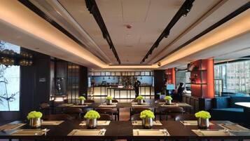 A modern restaurant with tables set for dining, a bar area in the background, and a view of the city.