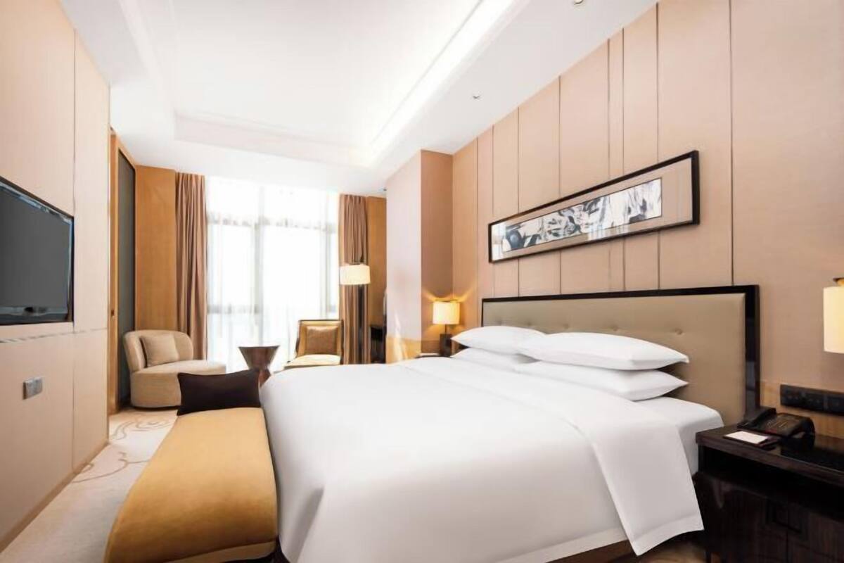 Habitación de hotel con una cama grande, un escritorio, una silla, un televisor y un cuadro en la pared.