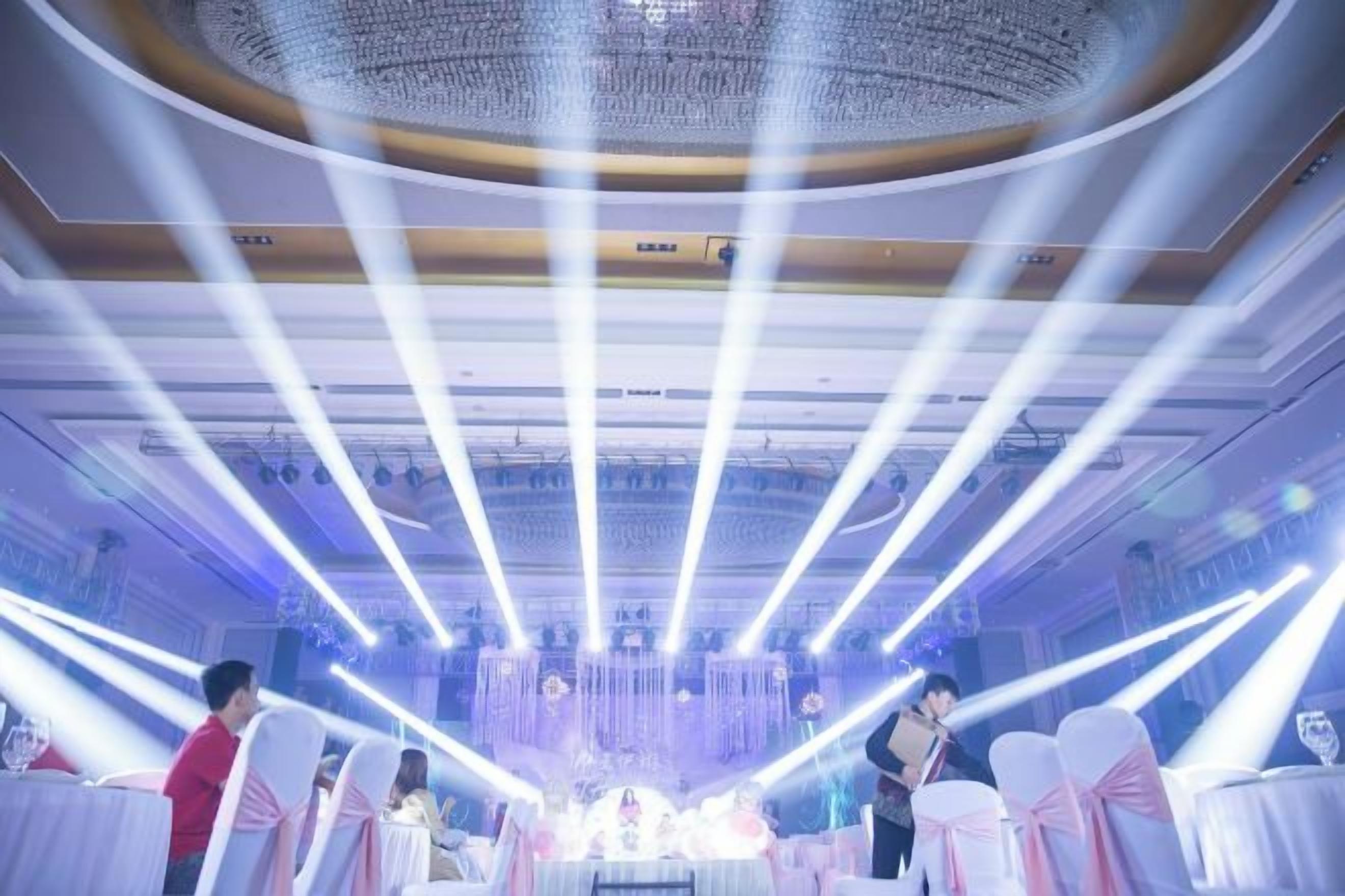 A banquet hall with tables set for a formal event, featuring a chandelier and overhead lighting.