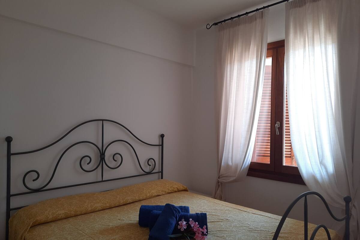 A bedroom with a bed, a window with curtains, and a metal headboard.