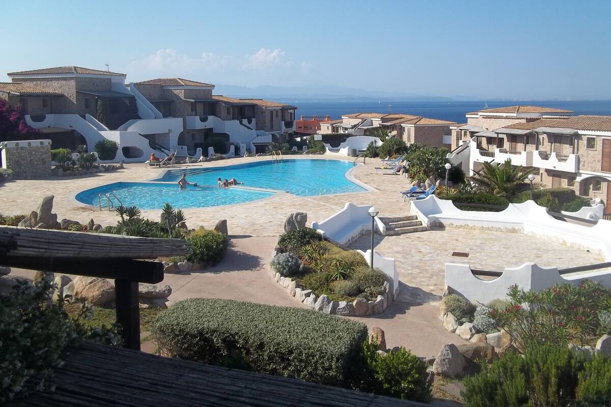 A resort with a large swimming pool, stone buildings, and a view of the sea.