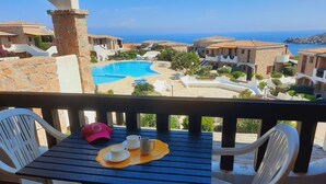 Uma varanda com mesa, cadeiras e vista para uma piscina e edifícios.