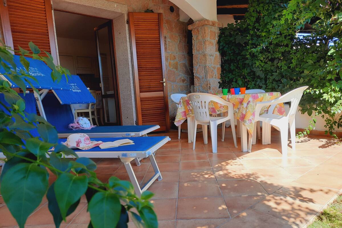 An outdoor seating area with lounge chairs and a table, a stone wall, and a door leading to an interior space.