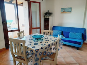 Un coin repas avec une table et des chaises, un canapé bleu et une vue à travers une porte vitrée.