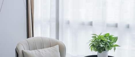 A room with a window, a chair, a small round table with a plant, and a lamp.