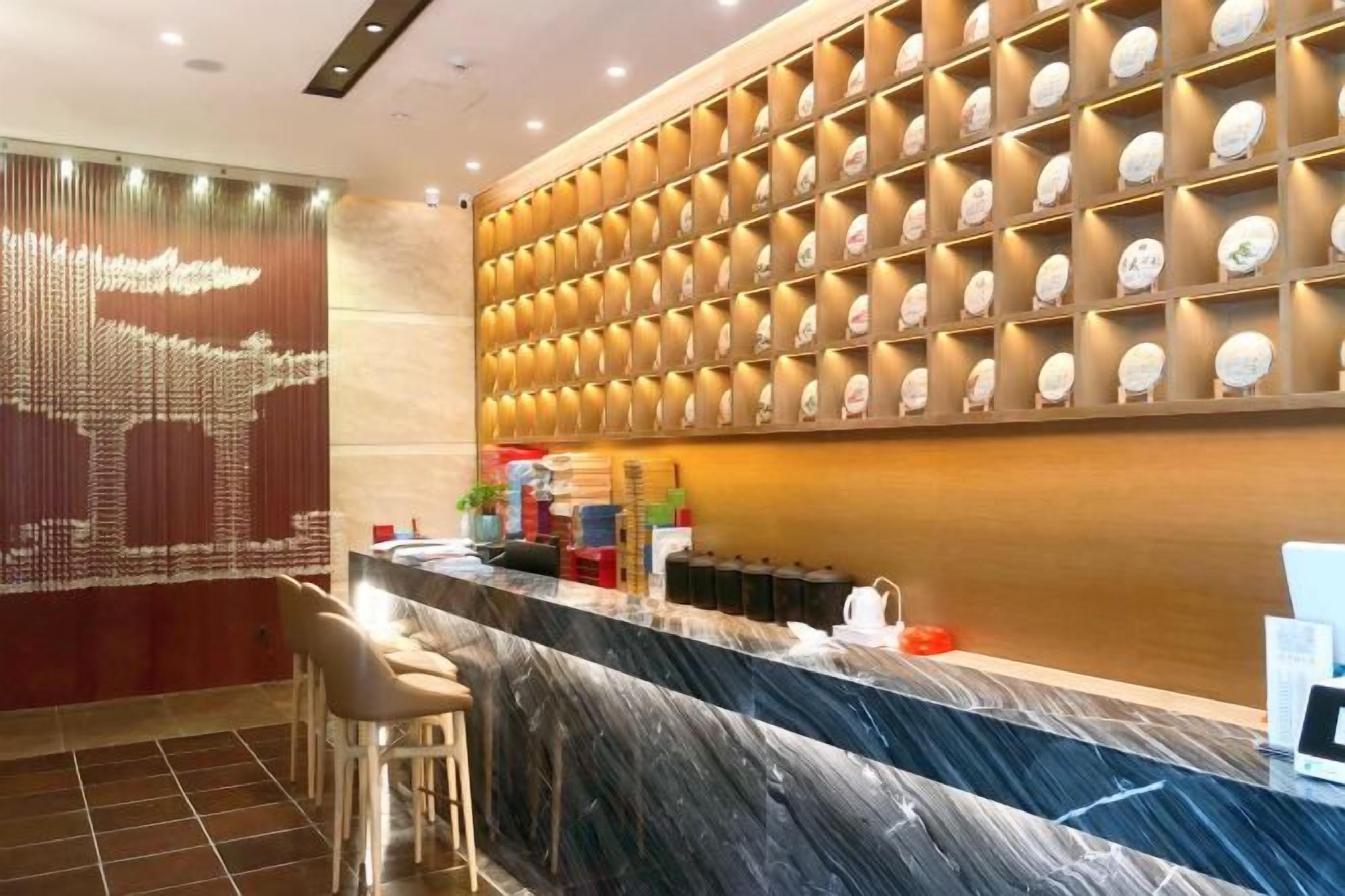 Uma área de recepção de hotel com balcão de mármore, uma parede com luminárias circulares e uma parede decorativa com padrão geométrico.