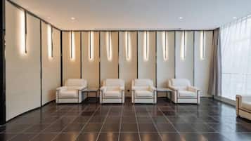 A modern waiting area with four white chairs, a dark tiled floor, and vertical light fixtures on the wall.