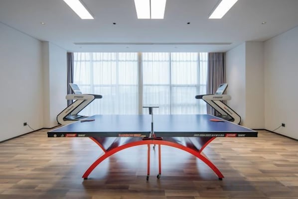 A ping pong table in a room with large windows, a treadmill, and a desk.