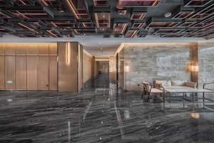 Un moderno vestíbulo de hotel con un suelo de mármol reflectante, un área de descanso con sillas y una mesa, y una pared divisoria de madera.