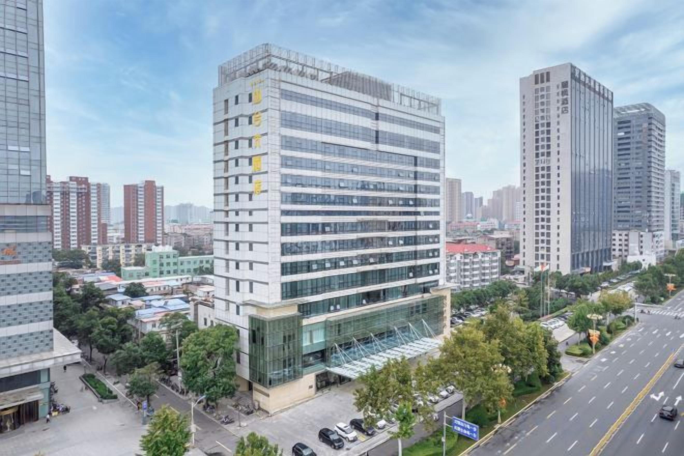 Un edificio de varios pisos con fachada moderna de vidrio, rodeado de otros edificios altos en un entorno urbano.