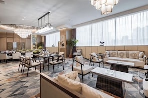 A hotel lobby with a dining area, seating arrangements, and large windows.
