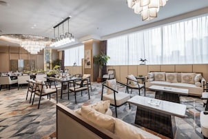 Un vestíbulo de hotel con zona de comedor, arreglos de asientos y ventanas amplias.