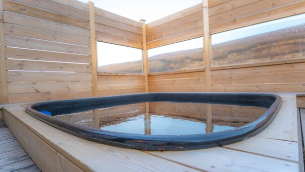 A wooden hot tub with a view of a hilly landscape. - Geldingsá Apartment (Akureyri)