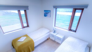 A room with two beds, a small bedside table, a nightstand, and a window with a view of the sea. - Geldingsá Apartment (Akureyri)