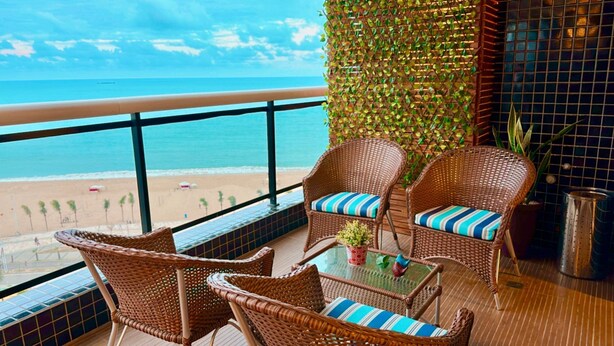 A balcony with wicker chairs and a table, overlooking a beach with a clear view of the ocean. - Landscape Beira Mar Platinum (Fortaleza)