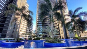A modern high-rise building with a pool area featuring palm trees and a clear blue sky. - Landscape Beira Mar Platinum (Fortaleza)