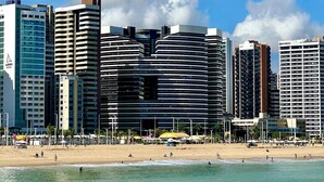 A beachfront hotel with multiple high-rise buildings in the background, a sandy beach, and clear blue skies. - Landscape Beira Mar Platinum (Fortaleza)
