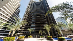 A modern high-rise building with a curved facade, surrounded by palm trees and well-maintained landscaping. - Landscape Beira Mar Platinum (Fortaleza)