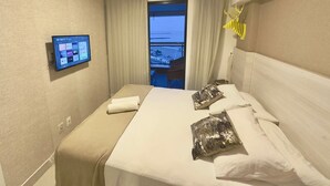 A hotel room with a bed, a mounted TV displaying streaming services, a view of the sea through the window, and an air conditioning unit. - Landscape Beira Mar Platinum (Fortaleza)